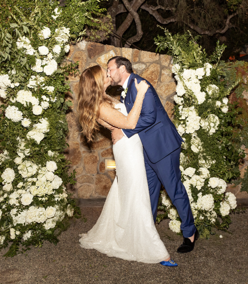 couple kiss and dip in front of white floral arch