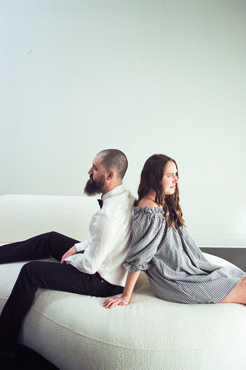 A couple sitting back to back wearing black and white, representing a styled photoshoot by Among the Oaks. 