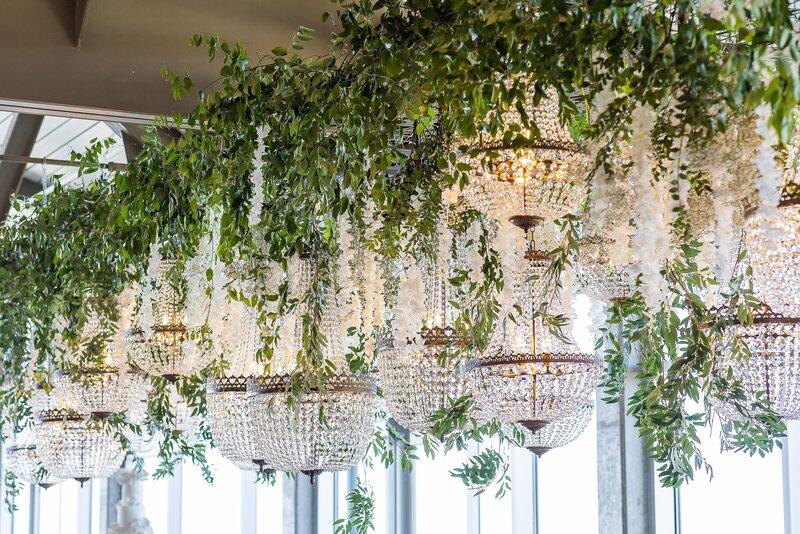 Chandelier and greenery decor hanging from the ceiling at a wedding reception