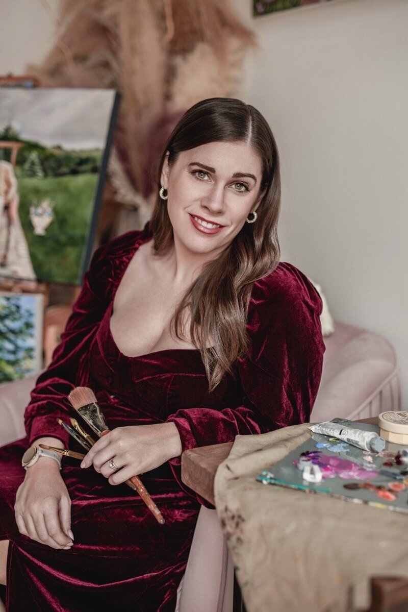 A headshot photo of Debbie smiling at the camera and holding paintbrushes