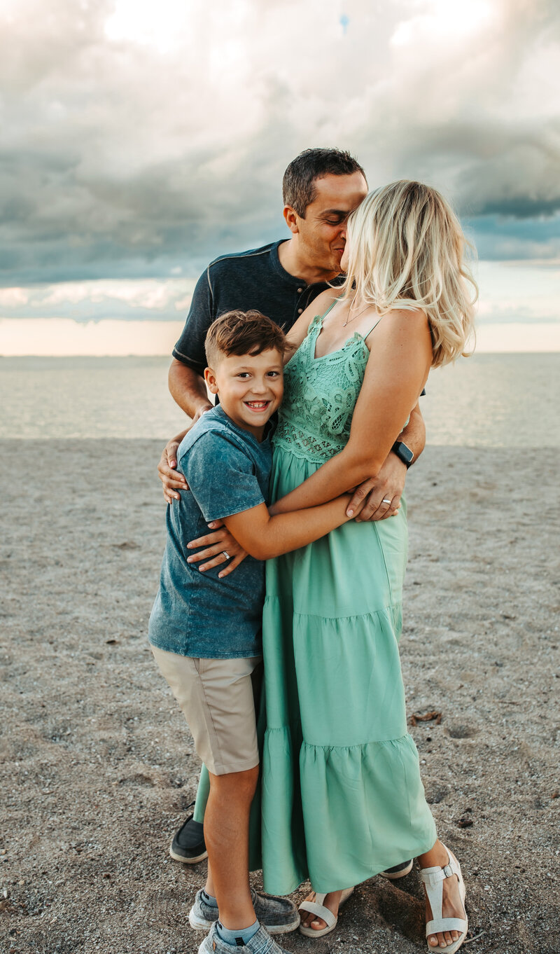 family picture of 3, parent kissing, boy looking at the camera on the beach in Maumee Bay in Toledo