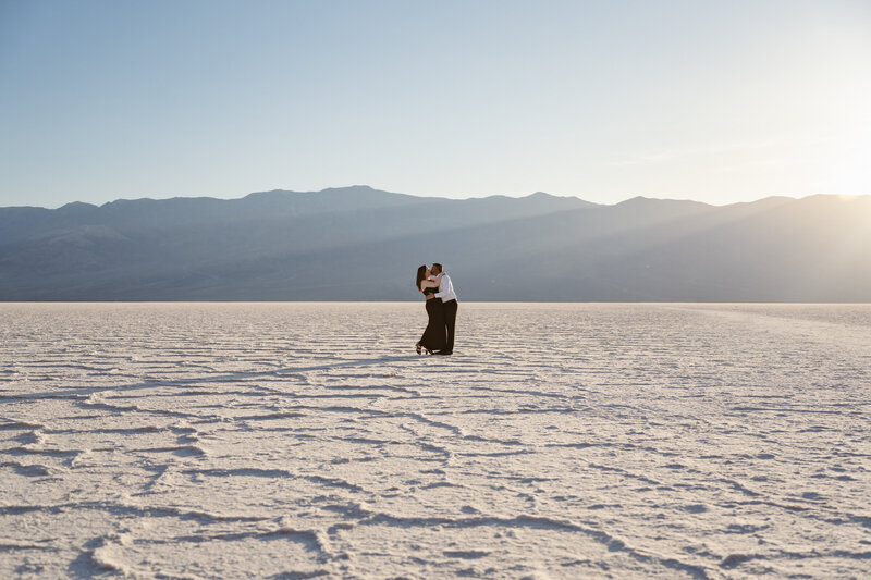 A couple kisses on the salt flats as the sun sets behind them, creating cinematic rays