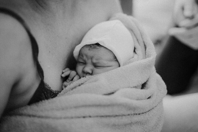 En nyfödd bebis vilar i mammas famn under en förlossningsfotografering i Göteborg