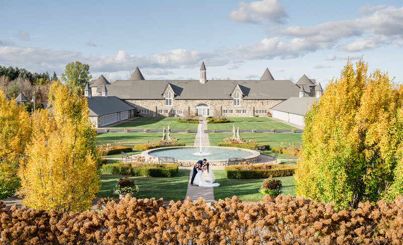 A groom dips his bride at a fall wedding with colorful trees in front of a Castle in Charlevoix