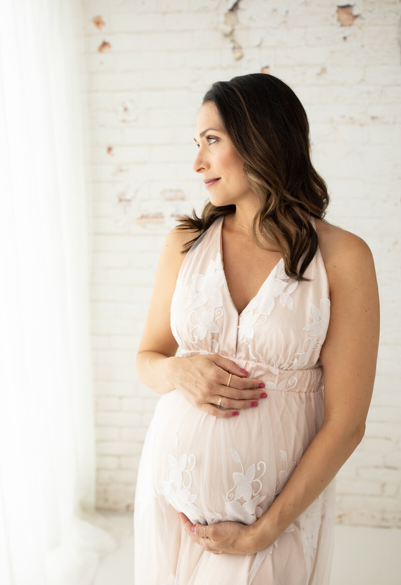 pregnant mom in cream maternity gown holding baby bump for studio maternity photoshoot cleveland family photographer
