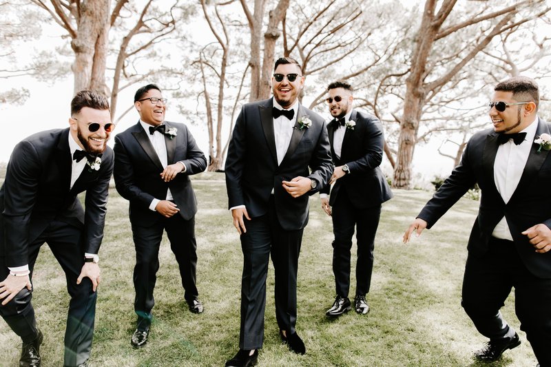 groomsmen in matching black tuxes laughing together