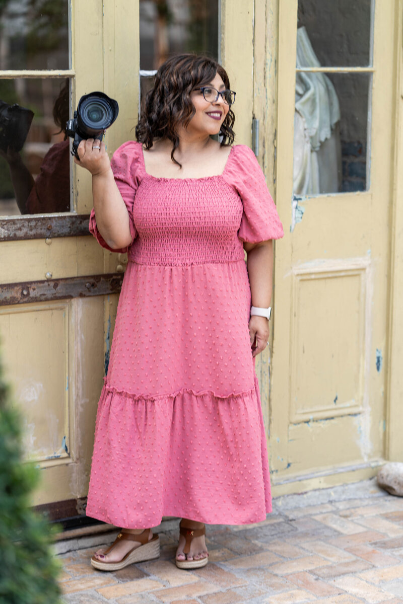Photographer wearing long mauve dress holding camera and looking into the distance  at Race and Religious in New Orleans.
