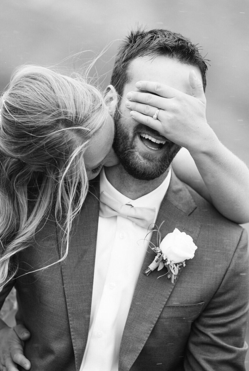 In this playful moment, the bride laughs beside the groom as he covers his eyes, capturing a spontaneous and joyful interaction on their wedding day. The photo exudes warmth and happiness, reflecting their deep connection and the light-hearted spirit of their celebration.