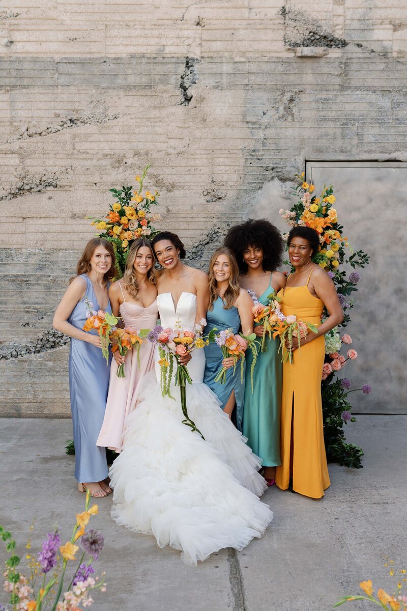 Bride poses with bridesmaids in colorful dresses at historic Phoenix wedding venue. 