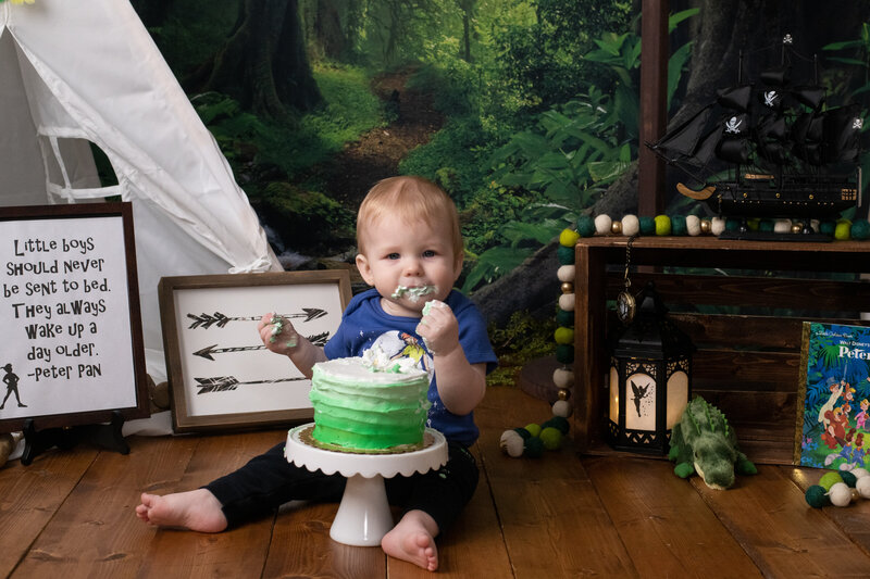 Peter Pan themed cake smash set with toddler eating a green birthday cake