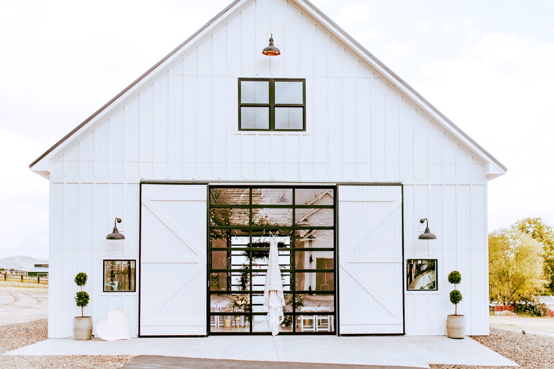 Front door of white barn with dress hanging on glass door.