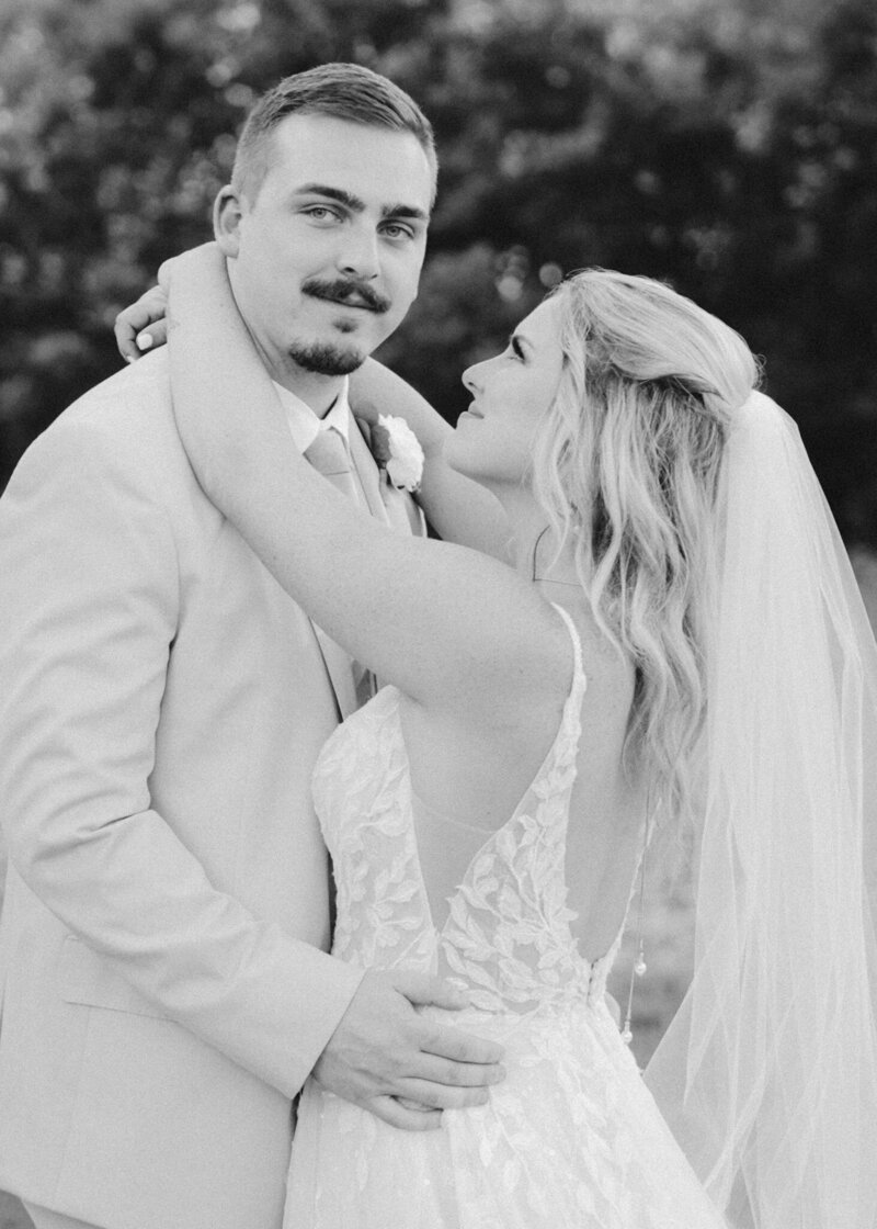 Black-and-white photo of a bride and groom embracing during their wedding, captured by Jacksonville-based wedding videographers, Tyler and Makenzie Films.