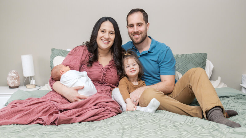 Parents posing at home with their daughter and newborn son during a lifestyle newborn photography session in Bergen County, NJ.