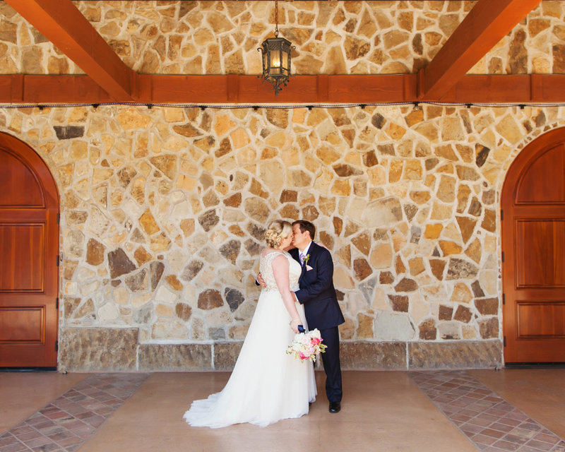 Full body portrait of Groom holding Bride kissing her