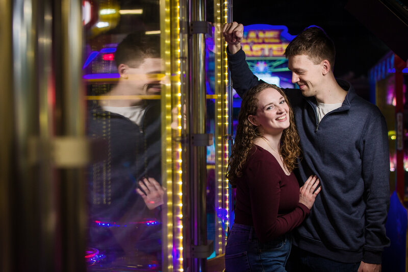 Couple sharing playful moments surrounded by neon lights and nostalgic arcade games during their quirky engagement session.