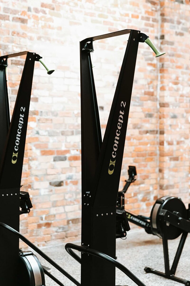 "Erg machines lined up in a well-lit East Brunswick gym with exposed brick walls and high ceilings."