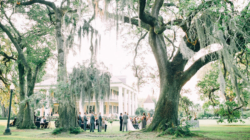 Outdoor wedding ceremony beside a large house and oak trees