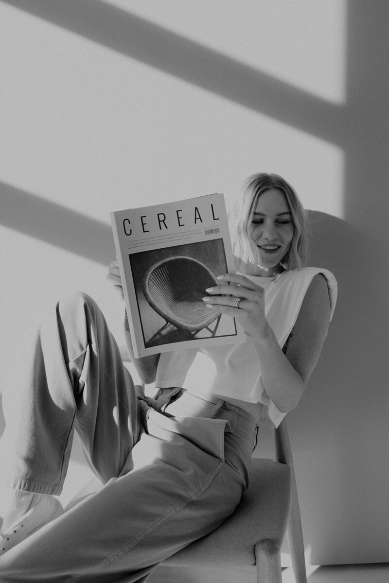 Black and white photo of Delcy Garnaas holding up Cereal Magazine while sitting in a chair