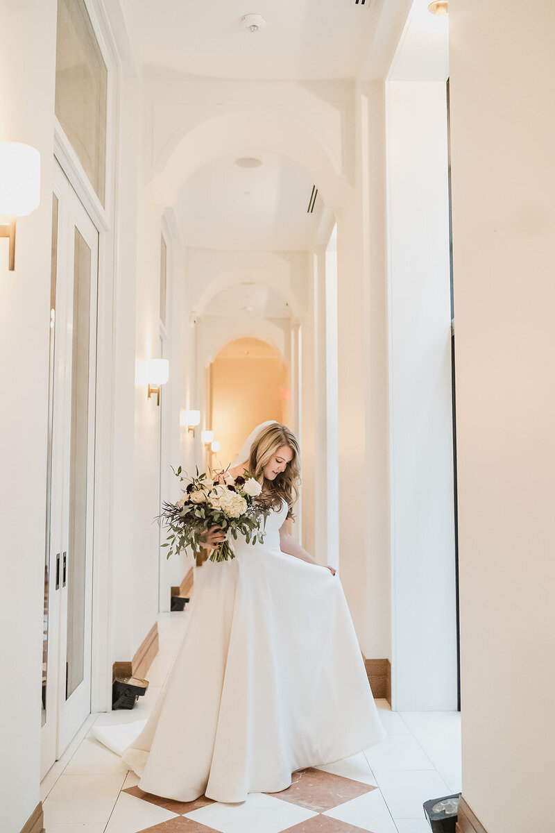 a  bride walks calmly through her wedding ceremony, captured candidly in black and white with her bouquet in hand and guests looking on.