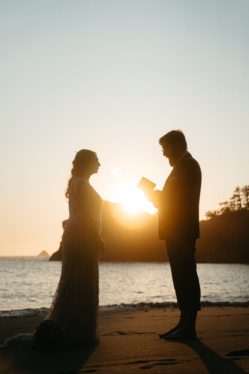 Eloping Ideas | Eloping groom reads his vows to his bride, illuminated by the golden sunset