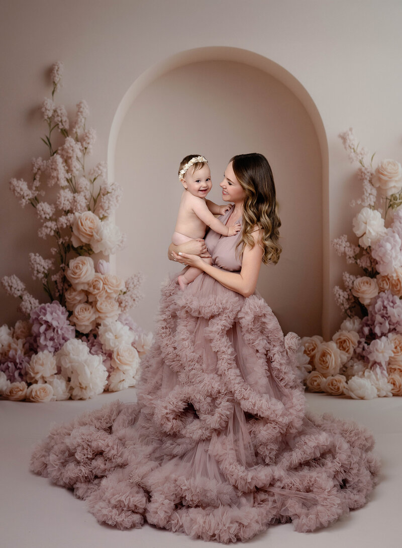 Mom looking at baby smiling. Mom is dressed in fine art gown. Mommy and me photo taken by Jenni Nikki at Atlanta Photo Studio.