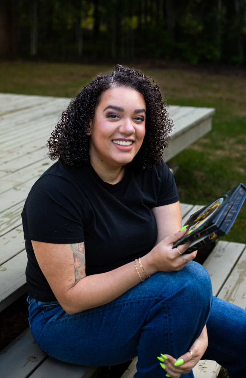 Fariss Hogue-Ziao, founder of Land of Birch book marketing agency, holding stack of fantasy romance novels