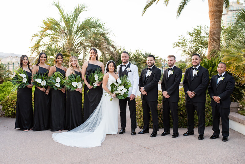 Bridal party in black and white attire posing with the couple in the lush courtyard.