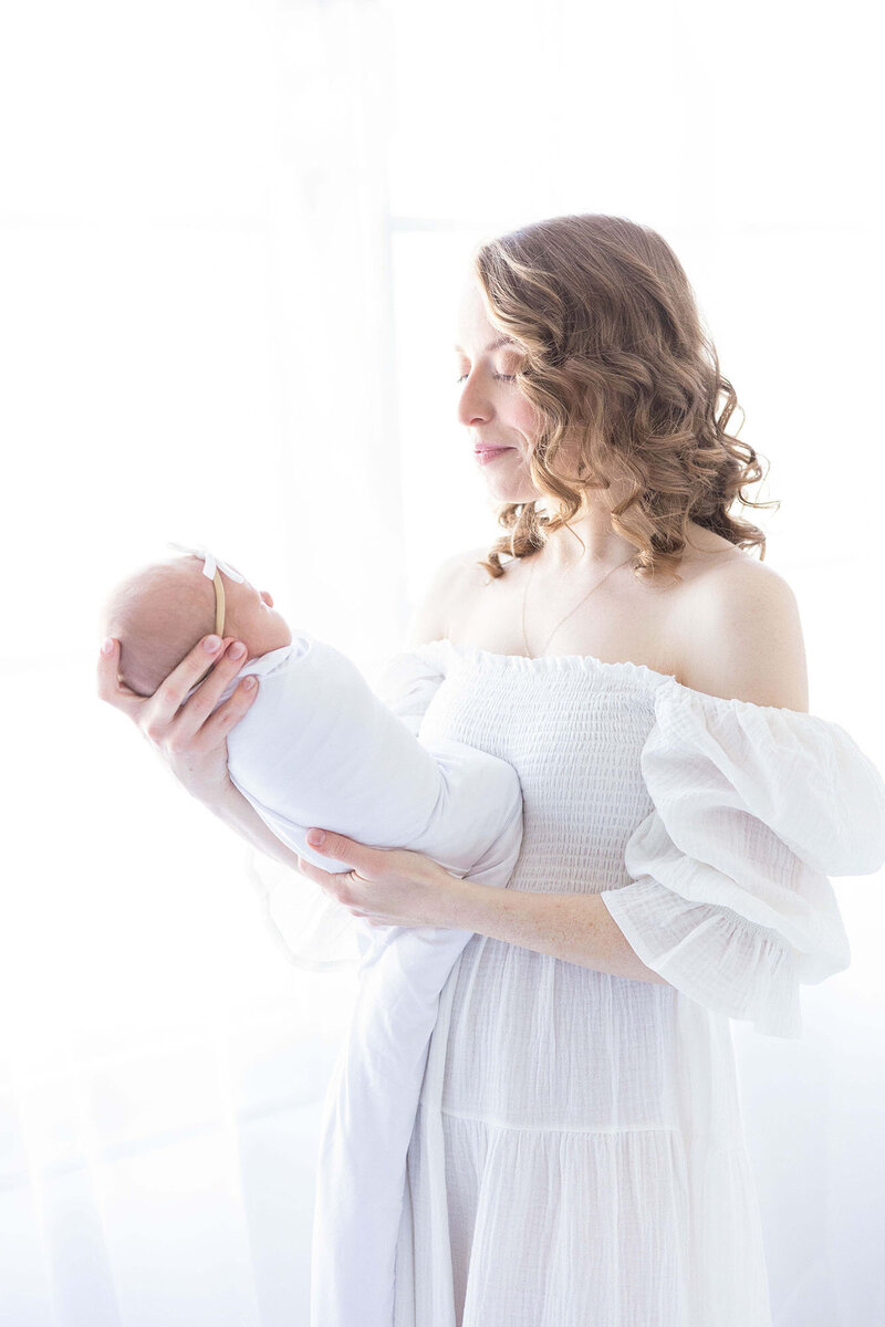 Mother in a white Nothing Fits But dress looking at her newborn baby with NH Newborn photographer Kathleen Jablonski