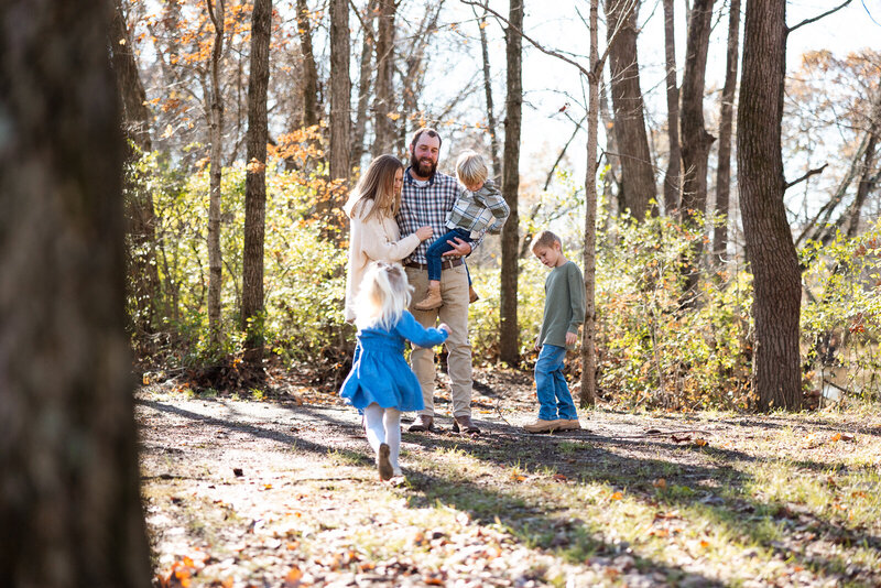 Family portrait with kids running around parents taken in the woods. 