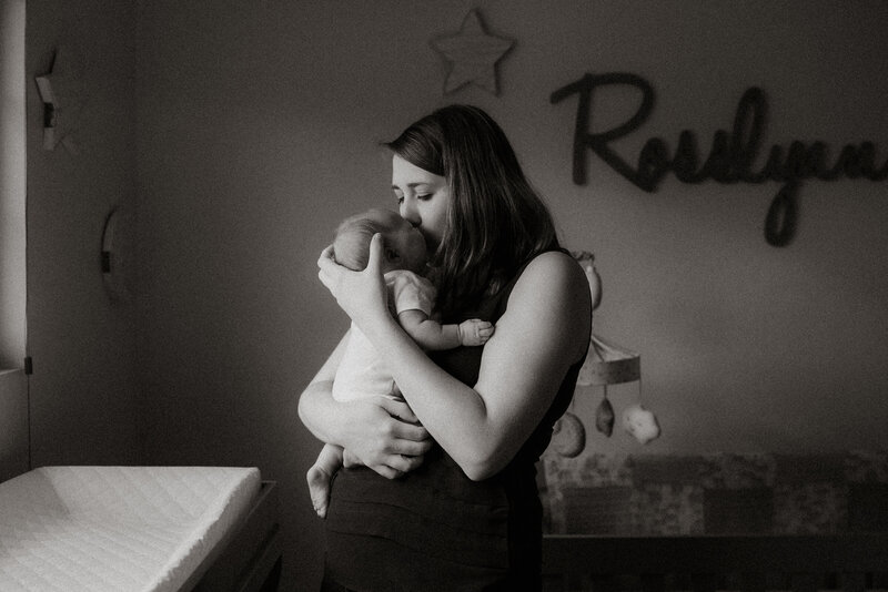 Black and white photo of a mother gently kissing her newborn in the nursery, captured during a cozy in-home newborn session in Irvine, California.