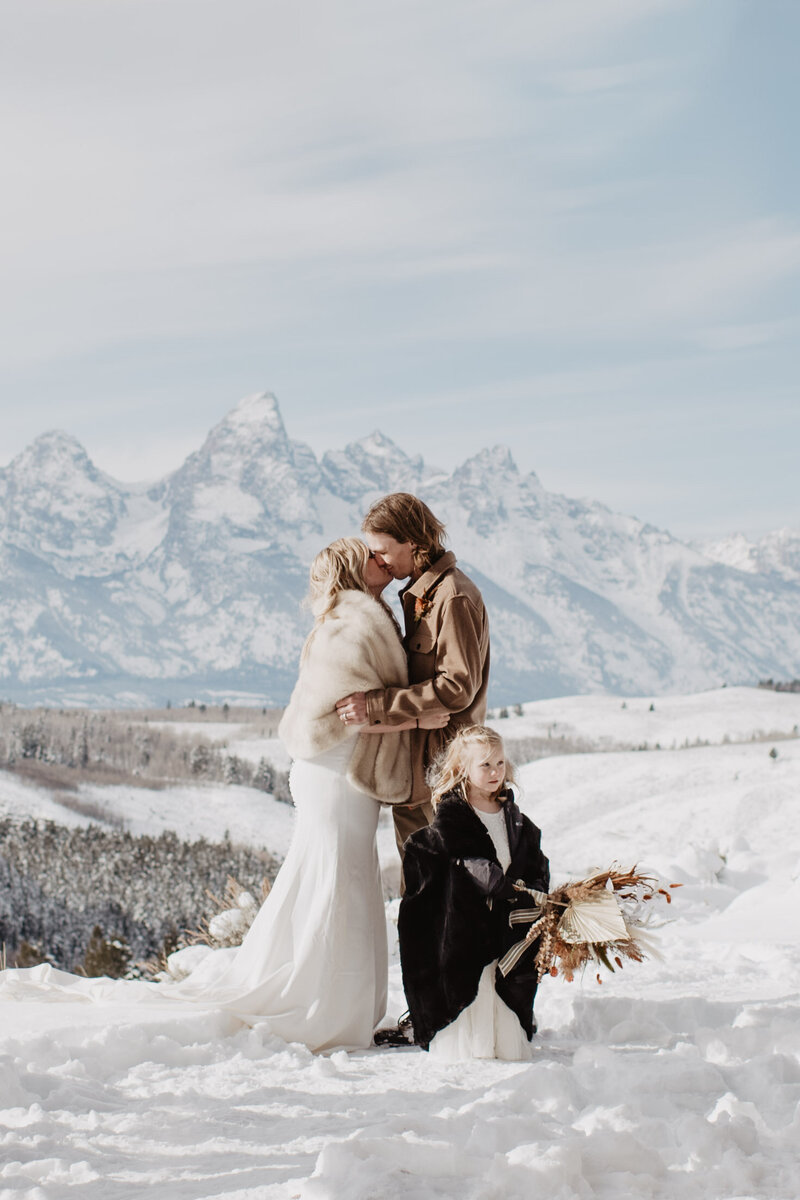 grand teton wedding ceremony in the winter with couple kissing on a mountain outlook with snow covered mountains photographed by photographers jackson hole