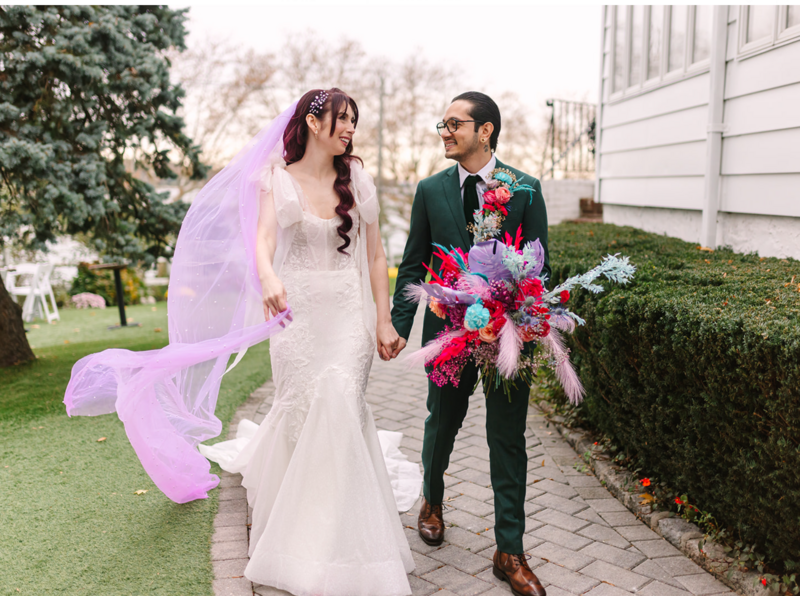 A bride with pink veil and groom in green tux holding  a colorful wedding bouquet.