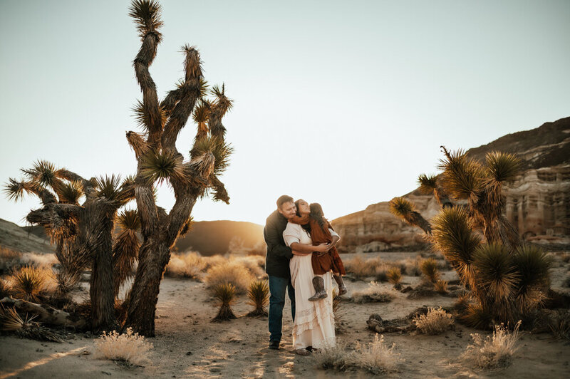 Family hugging near large cacti at sunset.