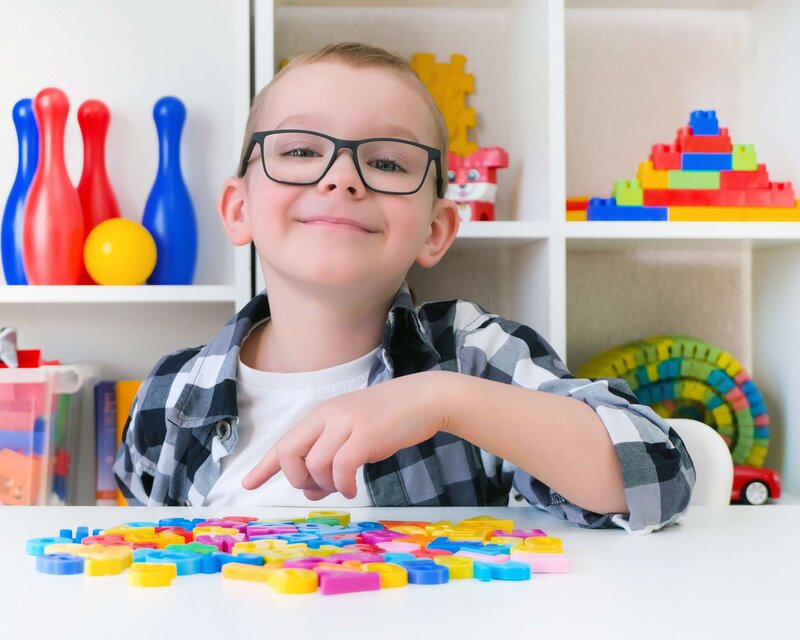 A school aged boy working on speech therapy exercises in a bright therapy room with small letters.