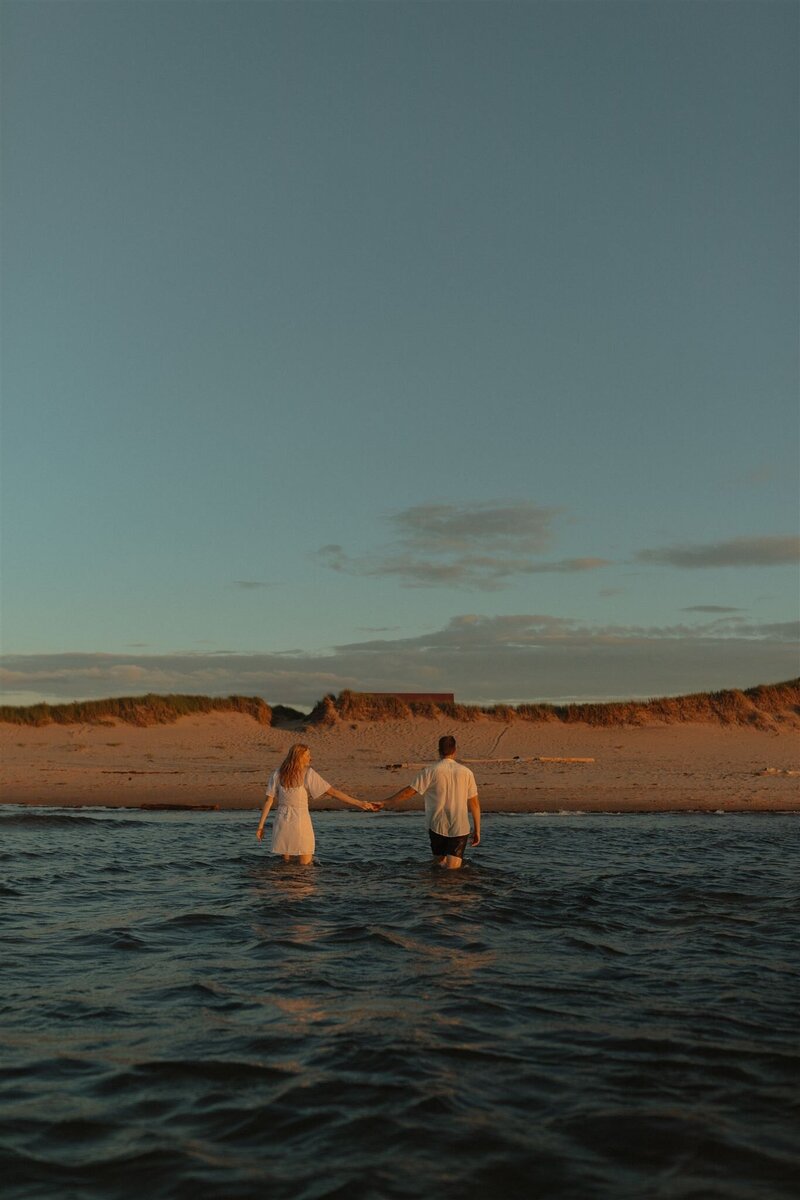 couple holding hands in ocean for lifestyle session in prince edward island