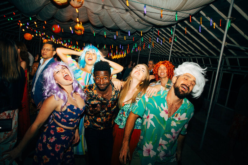 Wedding guests show off their smiles and dance moves while wearing colorful costumes at the coastal wedding venue Dos Pueblos Orchid Farm.