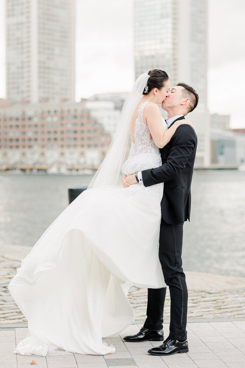 Groom picking up and kissing bride  at Fan Pier Park in Boston, MA