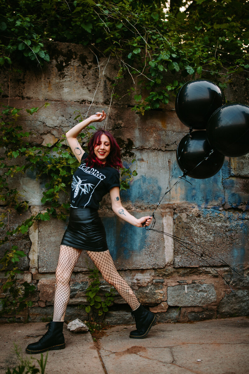 New England wedding photographer Andrea Van Orsouw posing playfully in fishnets and boots with black balloons, showing off her bold and alternative personality