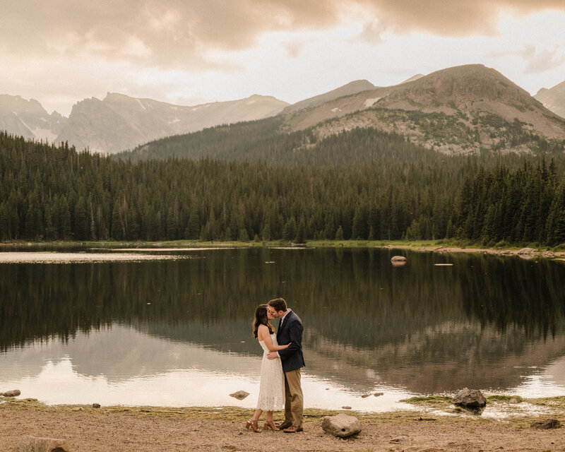 Couple kisses in front of a lake in the mountains of Colorado