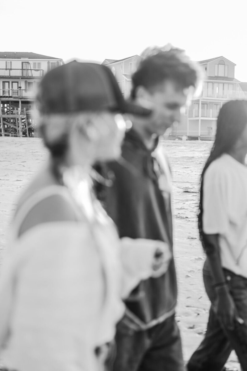 a black and white photograph of three baristas walking on the beach with an edgy vibe
