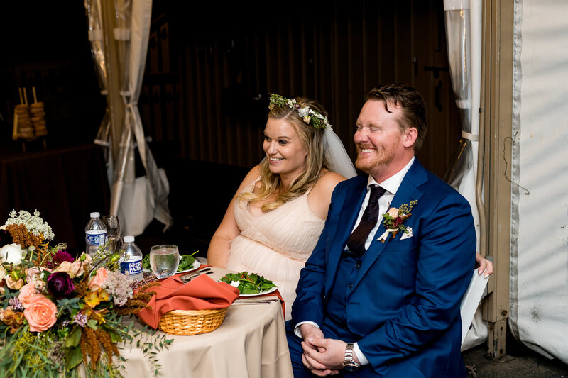 bride and groom laughter at their wedding reception. Groom is wearing a blue suit and the bride is wearing a blush pink dress.