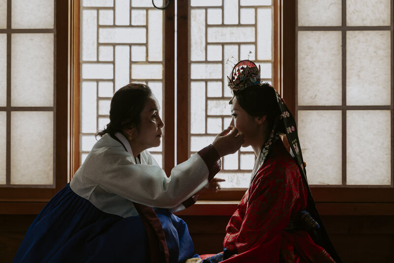 a Korean bride wearing traditional Korean clothes sits with her mom