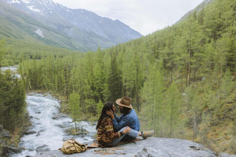 Couple embracing while sitting  with river and mountain in background.