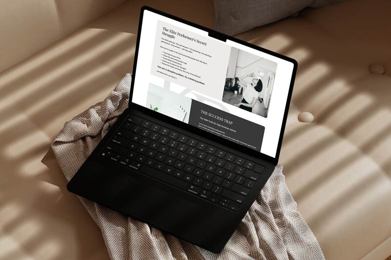 Open laptop resting on a beige couch, displaying a website with a black-and-white photo of a woman drinking from a cup and text about elite performers' struggles and success traps.
