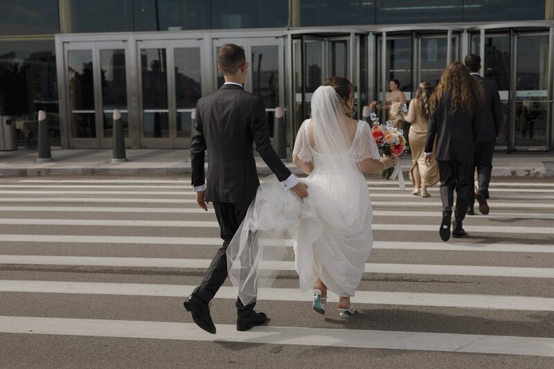 groom holding brides train as they cross the strees