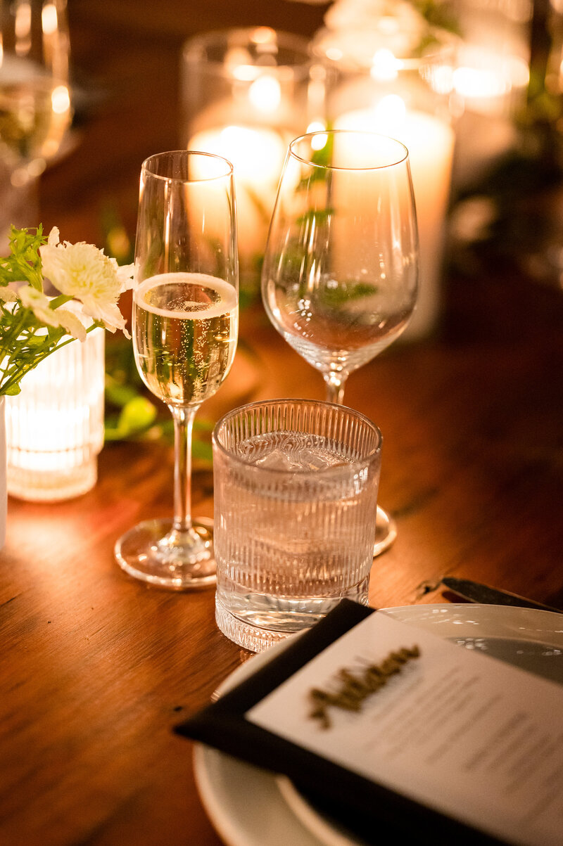 Candlelit table with a glass of champagne and a glass of water beside a wedding reception menu at Lilah in Philadelphia PA. 