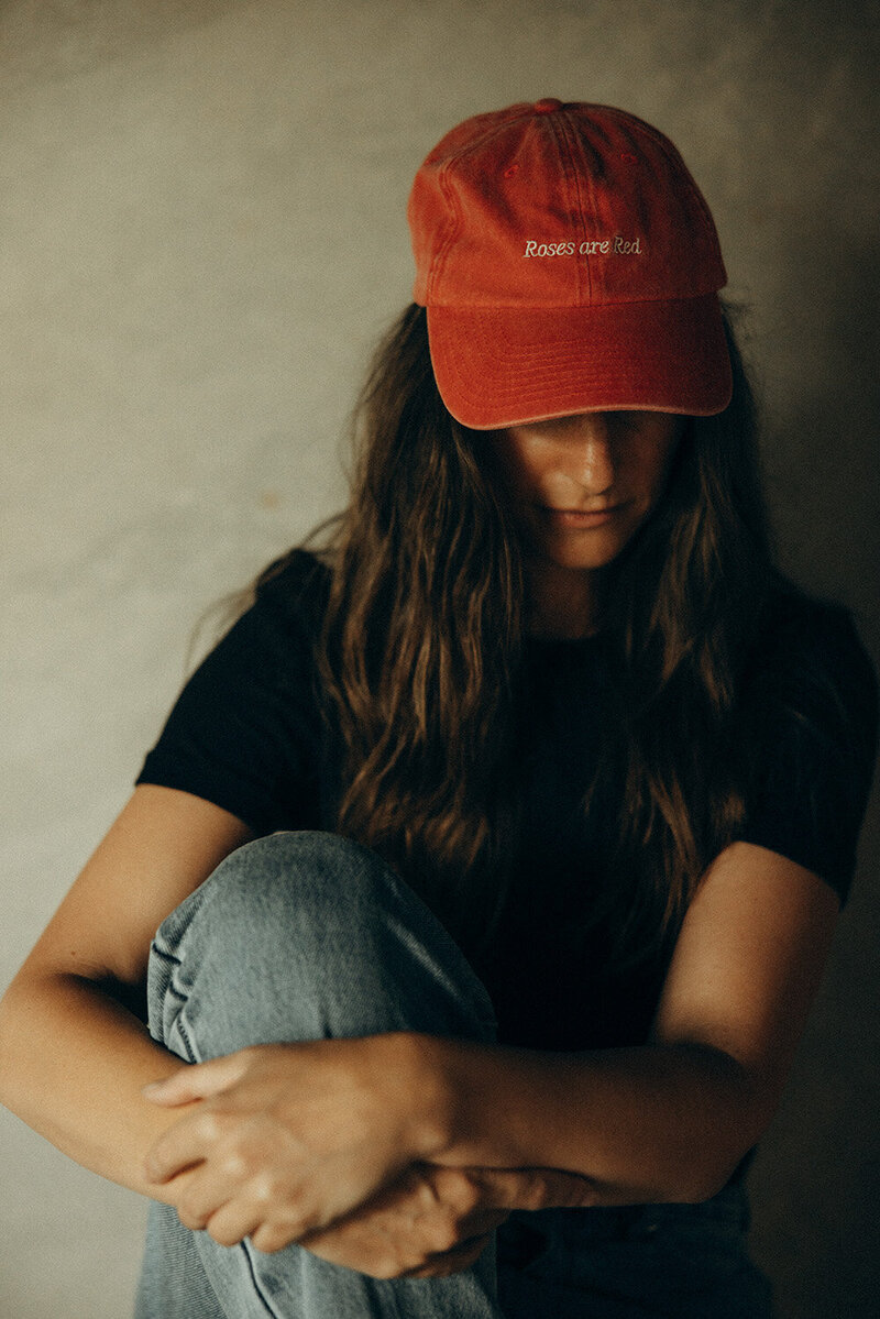 Personal branding photography with warm, earthy tones, featuring a woman in a red cap with 'Roses Are Red' embroidery, captured in an intimate storytelling session.