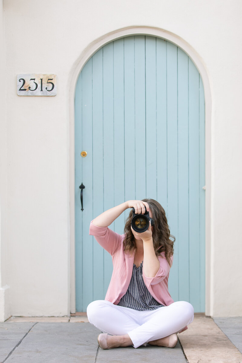 woman taking photo with camera sitting cross-legged on the ground in front of arched door