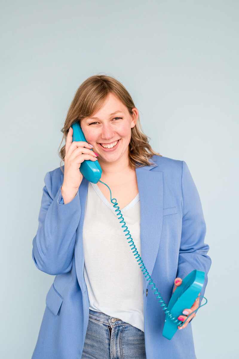 Kat Murphy in a blue blazer holding up a blue cord phone to her ear