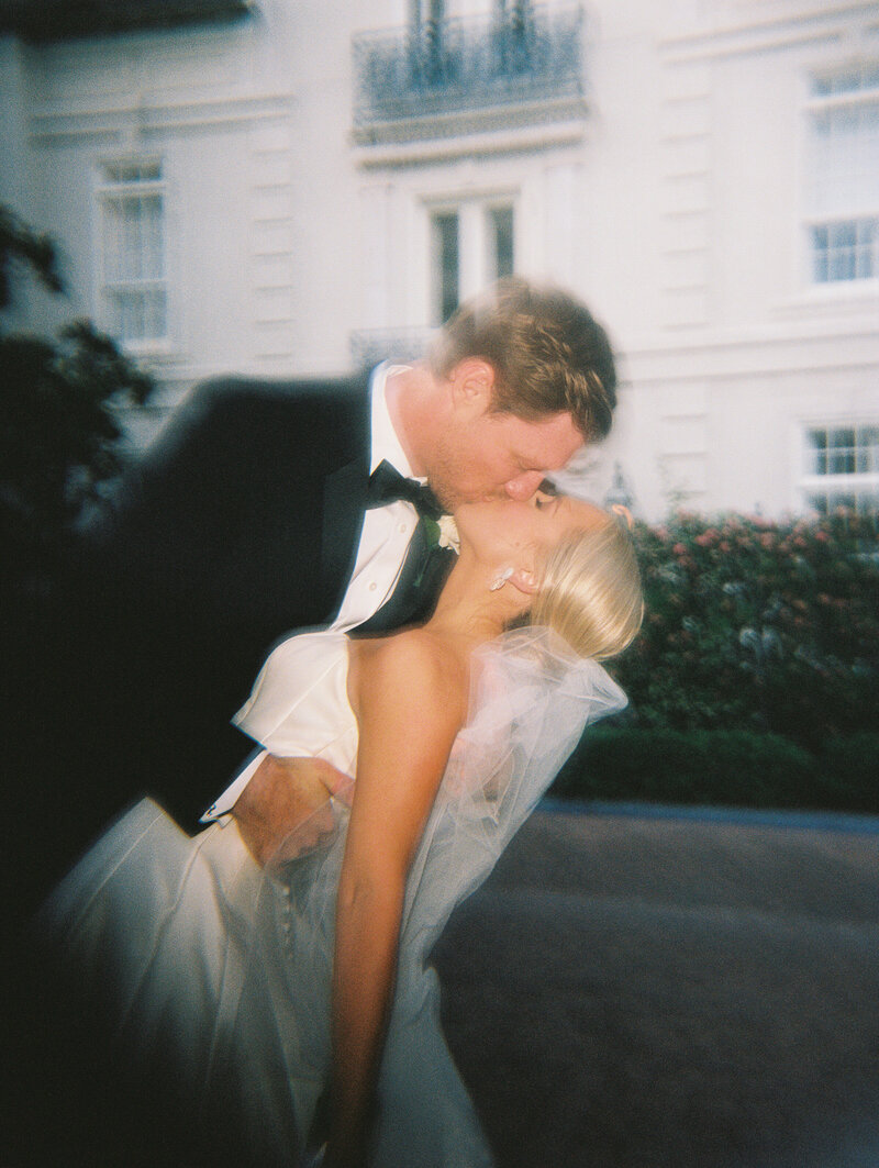 Film photo of bride and groom kissing with building in the background